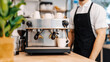 © Anucha - barista stands behind a professional espresso machine preparing coffee in a modern cafe setting.