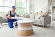 © Pixel-Shot - Male worker wrapping rattan table with stretch film in room