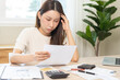 © KMPZZZ - Debt and financial concept, stressed asian young woman have a headache while female calculate expenses, income and expenses, looking bills of credit card for payment or payday on table at home office.
