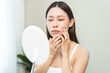 © KMPZZZ - Anti aging, worry puberty asian young woman, stressed girl looking in mirror, allergy presenting an allergic reaction from cosmetic on face. Beauty, health care from acne problem, dry skin, treatment.