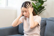 © KMPZZZ - Depressed anxiety asian young woman frustrated hand on head, touching her temples, suffering stressed, sick, tired, crisis on sofa from headache, migraine pain tension problem health care concept.