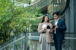 © Yingyaipumi - Business colleagues businessman and woman sitting and discussing,planning work using tablet outside office.City meeting and laptop with business people outdoor urban and green area for collaboration