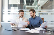 © Liubomir - Two business colleagues working together, discussing documents and analyzing data during a corporate meeting in a contemporary office setting, demonstrating teamwork and partnership