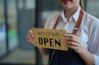 © Tj - Business owner holding welcome open sign for shop