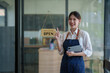 © Tj - Female small business owner welcoming customers to her open cafe