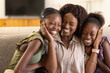 © Wavebreak Media - African American family mother hugging daughters while sitting on sofa at home showing smartwatch