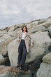 © SHOTPRIME STUDIO - Young woman in casual outfit stands confidently on rocky shore with cloudy sky. Concept of fashion, nature, outdoor lifestyle, and serene mood by the sea.