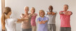 © Prostock-studio - A group of seniors participating in a stretching class with an instructor. They are following along, reaching their arms forward. The setting is bright and indoor, suggesting a morning event.
