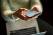 © Davor - Person texting on smartphone over laptop indoors