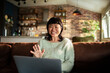 © Davor - Smiling woman waving during video call at home