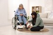 © New Africa - Caretaker helping senior woman in wheelchair putting on shoes at home