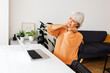 © Xavier Lorenzo - Tired stressed mature businesswoman suffering from neck pain working on laptop at home. Overworked senior middle aged lady massaging neck sitting on table working from living room