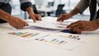 © Justlight - Retail client service staff organizing colorful investment growth graphs focused hands placing pages indistinct office environment behind.