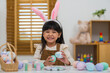© geargodz - happy preschool child girl wearing bunny ears holding colorful egg while celebrating on easter day on table at home
