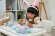 © geargodz - happy preschool child girl wearing bunny ears painting and decorating colorful egg at home on easter day