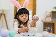 © geargodz - preschool child girl wearing bunny ears painting and decorating colorful egg at home on easter day