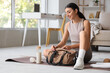 © Pixel-Shot - Sporty young woman with bottle of water and bag sitting on yoga mat at home
