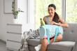 © Pixel-Shot - Sporty young woman with bottle of water in bag sitting on sofa at home