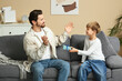 © Pixel-Shot - Little cute boy giving gift to his dad in living room. Father's day