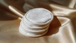 © Darya - Stack of white cotton pads on a beige satin fabric. the pads are arranged in a circular pattern, with the topmost pad being the smallest and the bottommost being the largest.