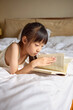 © Blue Jean Images - Girl lying on bed, reading a book