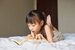 © Blue Jean Images - Girl lying on bed, reading a book