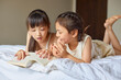 © Blue Jean Images - Sisters lying on bed, reading a book