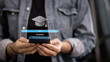 © จุฑารัตน์ เจริญวงษ์ - Person holding smartphone with 100 percent complete progress bar and graduation cap icon.