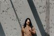 © Westend61 - Woman holding flower in front of eye while standing against concrete wall on sunny day