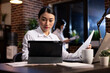© DC Studio - Dedicated female professional working late in corporate office, reviewing business reports on a tablet. Asian manager surrounded with digital devices on her desk, focused on project planning at night.