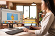 © DC Studio - Talented graphic editor adjusts design features and retouches images using drawing tablet. Asian female photographer updating portfolio, working precisely on visual content from home studio.
