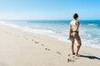 © Connect Images - Woman holding sandals stands on a sandy beach looking at the ocean under a clear blue sky.   Half Moon Bay, California, USA