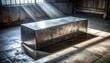 © Agusstudio - A large, dull grey block of pure lead rests heavily on a scuffed concrete floor, illuminated by dramatic sunbeams streaming through a window in an old industrial setting.