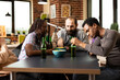 © DC Studio - Young male and female adults sit around table with beer and chips, looking bored in cozy room. Group of friends relax together in brick walled room, sharing snacks and drinks, feeling unoccupied.