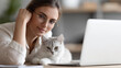 © Nataliya - Defocused unrecognizable young freelancer woman in eyeglasses working at home with a laptop and a cat, remote work, education, work from home concept, with copy space