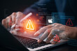 © IDOL'foto - Cybersecurity threat warning concept with developer analyzing system code on laptop while digital alert icon highlights network security risk data breach detection and cyberattack protection.