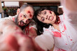 © DC Studio - Employees having fun in workplace dressed as zombies for Halloween event, taking selfies doing silly faces. Man and woman covered in fake wounds pretending to be reanimated corpses, doing photos, POV