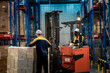 © ultramansk - Diverse industrial team communicating about successful freight delivery. Male warehouse worker operating forklift and giving thumbs up to colleague inspecting shrink wrapped pallet.
