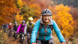 © Joyce - Cardio sports cycling biking exercise training, healthy lifestyle. A group of people riding bicycles down a trail in the fall. The woman in the foreground is wearing a blue jacket, gray pants.