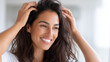 © Olha Havelia - A positive, high-key commercial shot of a smiling woman with healthy, voluminous dark hair, gently massaging her scalp with her fingertips in a sunlit room. Hair recovery, blood ci