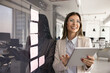 © fizkes - Happy businesswoman, project coordinator or marketing staff member holds tablet device stands near of wall with attached sticky notes smiling, reviewing sales results, enjoy workflow, chatting online