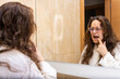 © Ivi - Powerlightss - Woman examining teeth in mirror during morning self-care routine