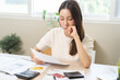 © KMPZZZ - Debt and financial concept, stressed asian young woman have a headache while female calculate expenses, income and expenses, looking bills of credit card for payment or payday on table at home office.