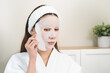 © KMPZZZ - Skin care beauty person concept. Asian young woman applying white cosmetic face mask, sheet pad for treatment moisturizing, relax spa and skin cosmetology. Lifestyle routine therapy of dermatology.