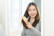 © KMPZZZ - Health hair care, beauty concept. Asian woman, girl holding hairbrush and brushing, combing her long straight hair looking at reflection at mirror in morning routine after hair and treatment at home.