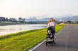© leungchopan - Mother pushing baby stroller through park at sunset
