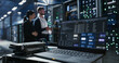 © Gorodenkoff - Laptop sits on a cart beside hard drives in data center.  Two people discuss network infrastructure and server maintenance among  server racks and mainframes.