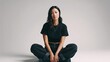 © Oleh - Young asian woman sitting with crossed legs on the floor, looking at the camera in a minimalist studio featuring natural makeup and casual black attire