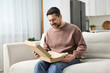 © New Africa - Happy man opening parcel on sofa at home
