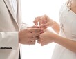 © Sarojah - Close-up of hands exchanging rings. A bride in a white gown and a groom in a cream suit exchange rings during a wedding ceremony